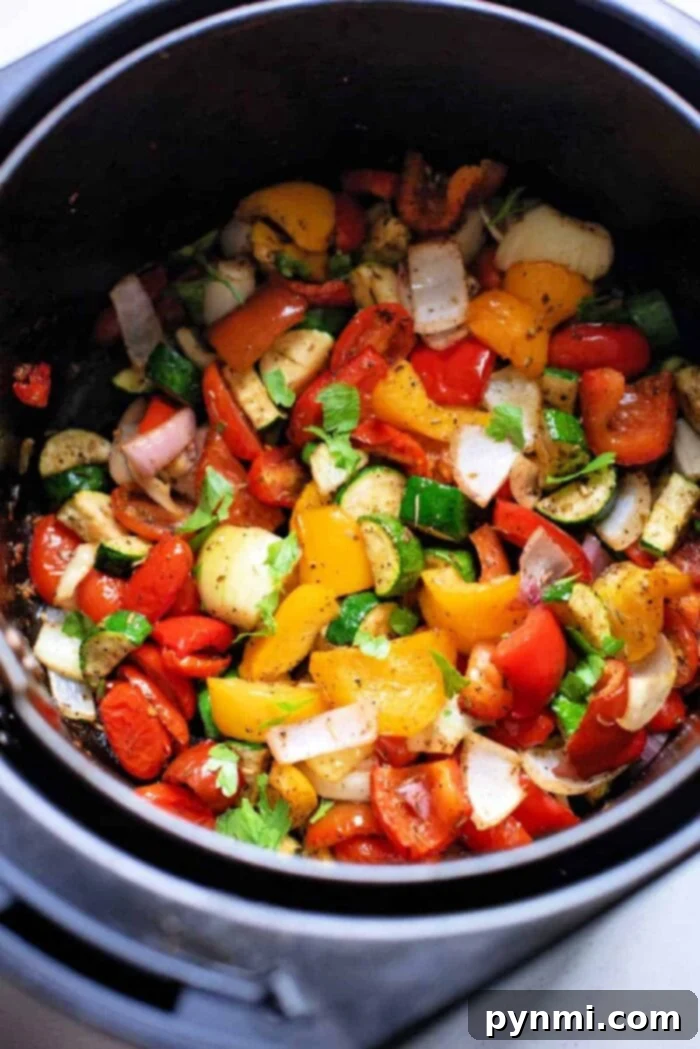 Air fryer basket brimming with vibrant chopped Mediterranean vegetables like peppers, onions, and zucchini, ready for roasting.