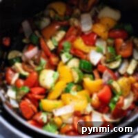 A vibrant mix of Mediterranean roast vegetables, including peppers, zucchini, onions, and herbs, nestled in a black pot, showcasing their perfectly charred and aromatic appearance.