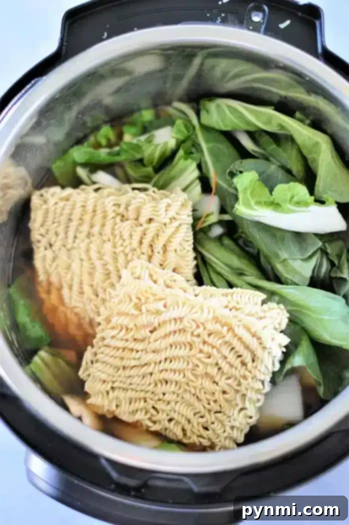Easy Instant Pot Ramen 8 The Instant Pot is filled with vibrant ingredients for a delectable vegetable ramen. Two blocks of dry instant noodles rest atop an assortment of fresh leafy greens and sliced roots, all simmering in the savory broth.