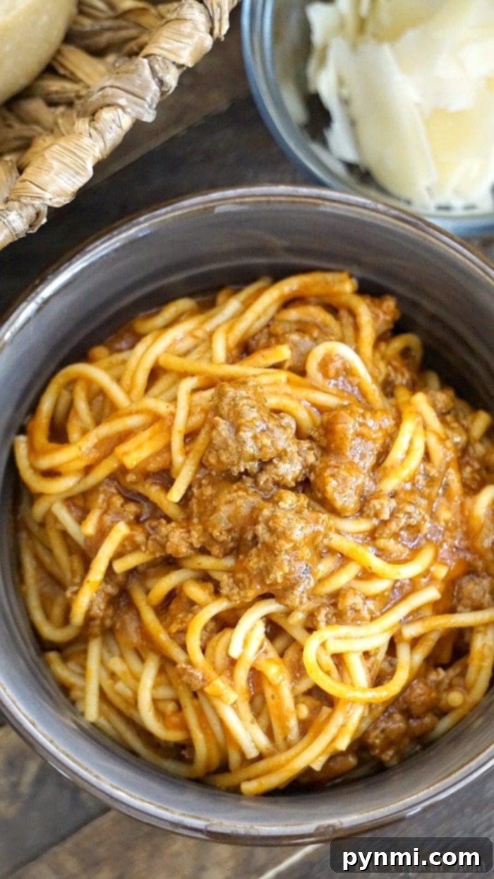 A bowl of instant pot spaghetti with savory meat sauce sits next to a delightful bowl of cheese and a charming wicker basket.