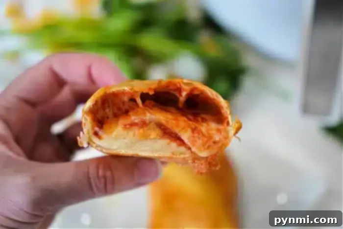 Perfecting Your Hot Pocket Cook Time 3 A hand is holding a partially bitten piece of a rolled and baked food item with a tomato sauce filling and melted cheese inside.