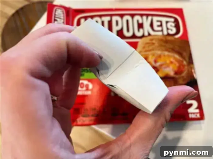 Perfecting Your Hot Pocket Cook Time 6 A hand holding an unfolded crisping sleeve with a Hot Pockets package in the background.