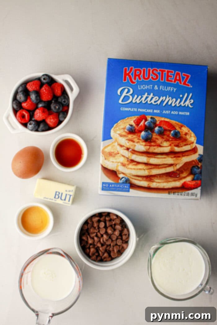 Box of pancake mix, berries, chocolate chips, butter, milk, egg, vanilla, and syrup on a gray surface—everything you need for delicious oven baked pancakes with pancake mix.