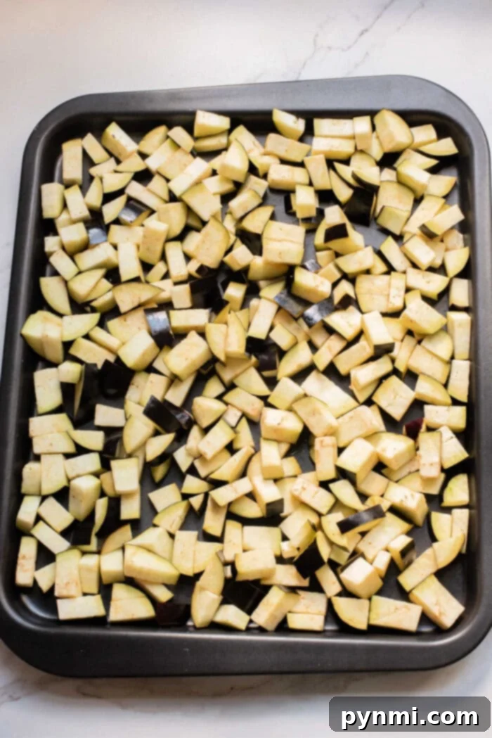 A baking tray filled with evenly spread, diced raw eggplant pieces on a light countertop—perfect for starting your favorite eggplant casserole or trying a new eggplant recipe.