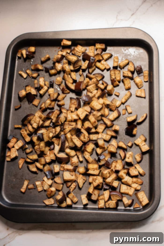 Chopped roasted eggplant pieces spread on a dark baking sheet hint at the perfect start to an irresistible eggplant casserole or your next favorite eggplant recipe.