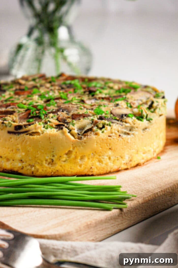 Pressure Cooker Quiche Perfection 6 A thick vegetable frittata, inspired by an Instant Pot quiche recipe, is topped with herbs and sits on a wooden board next to fresh chives.