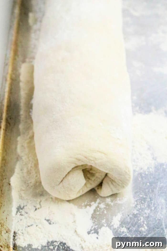 Rolled Philly Cheesesteak Stromboli dough log on a floured metal baking sheet, ready for baking.