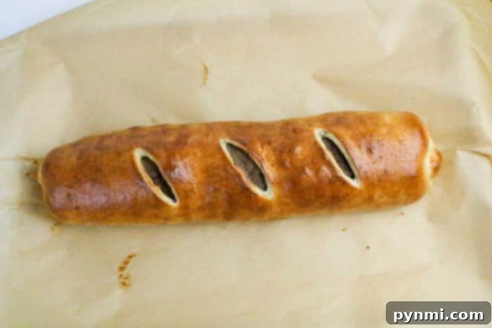 A golden-brown Philly Cheesesteak Stromboli baked pastry roll with three diagonal slits on top, resting on parchment paper.