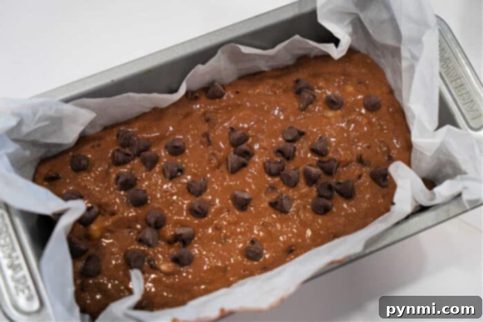 Chocolate Banana Bread batter with chocolate chips in a parchment-lined loaf pan.