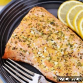 Baked frozen salmon fillet on a black plate with lemon slices and a fork, showing how deliciously simple it is to prepare frozen salmon in the oven.
