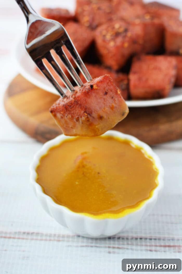 A cube of Bologna Burnt Ends being dipped in mustard sauce.
