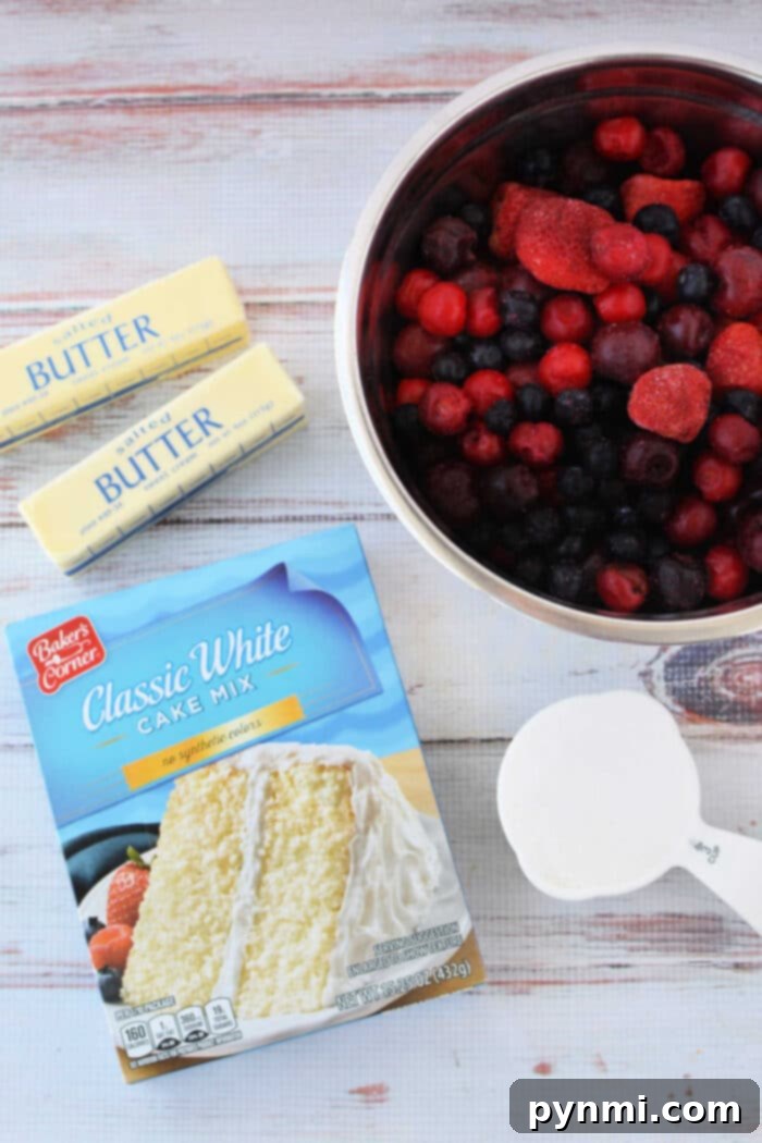 Cake Mix Berry Cobbler 3 A perfectly arranged flat lay showcasing the four essential ingredients for making Berry Cobbler with Cake Mix: a vibrant box of white cake mix, two sticks of softened butter, a generous bowl of frozen mixed berries, and a cup of granulated sugar, all set on a clean white surface.