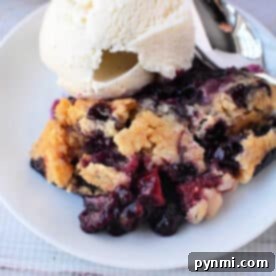 A plate with Berry Cobbler with Cake Mix and a scoop of vanilla ice cream, with a spoon beside them.