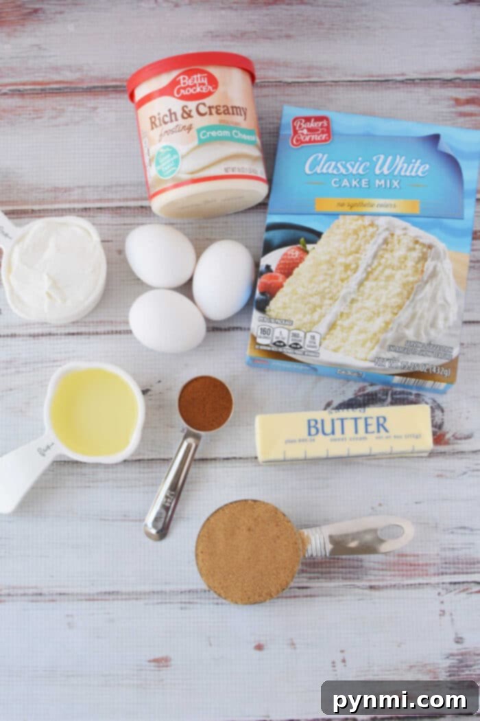 Semi-Homemade Cinnamon Roll Cake 3 A collection of ingredients artfully arranged on a white table, including a box of cake mix, fresh eggs, a tub of cream cheese frosting, sticks of butter, vegetable oil, sour cream, brown sugar, and cinnamon, all waiting to be transformed into a delicious cinnamon roll cake.