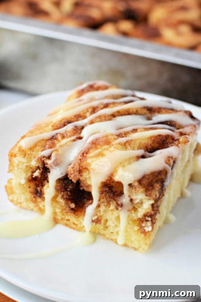 Semi-Homemade Cinnamon Roll Cake 6 A perfectly portioned slice of Cinnamon Roll Cake, generously adorned with a sweet, delicate icing drizzle, presented elegantly on a clean white plate, ready to be enjoyed.