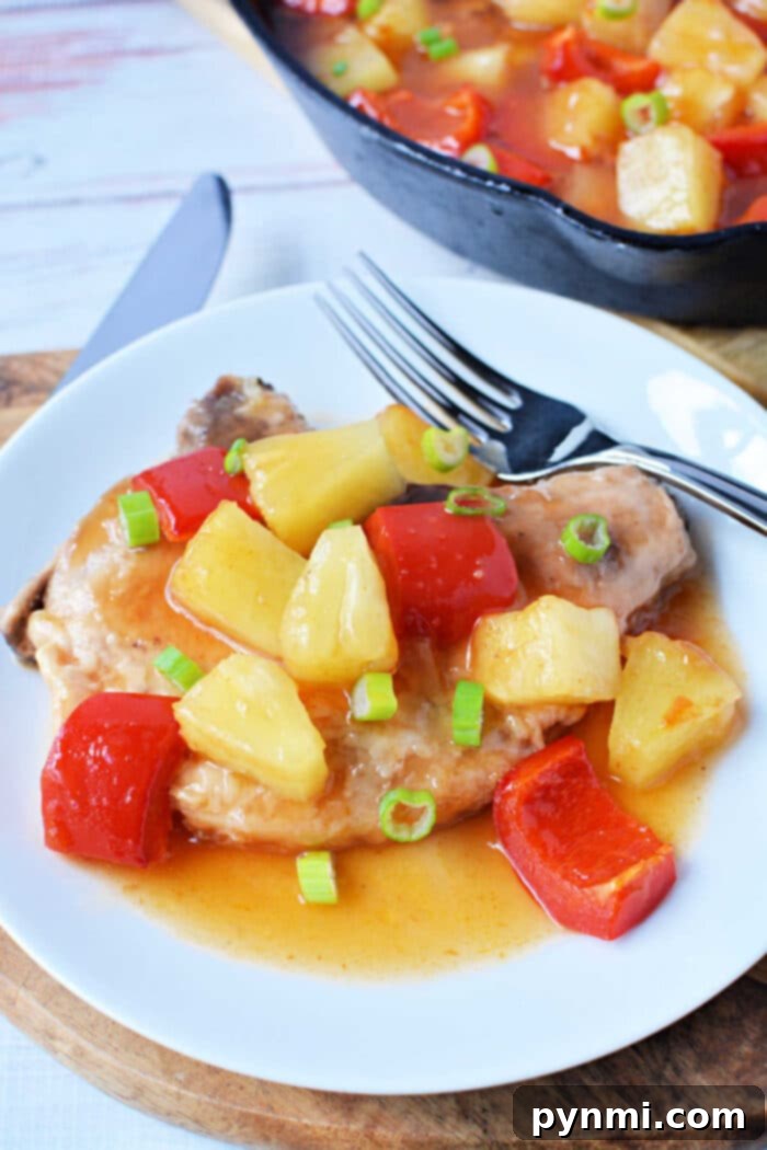 Tropical Pork Chops 2 This dish features succulent pork chops topped with pineapple, red bell peppers, and sauce, then garnished with green onions on a white plate. A vibrant addition to your collection of pork chop recipes.