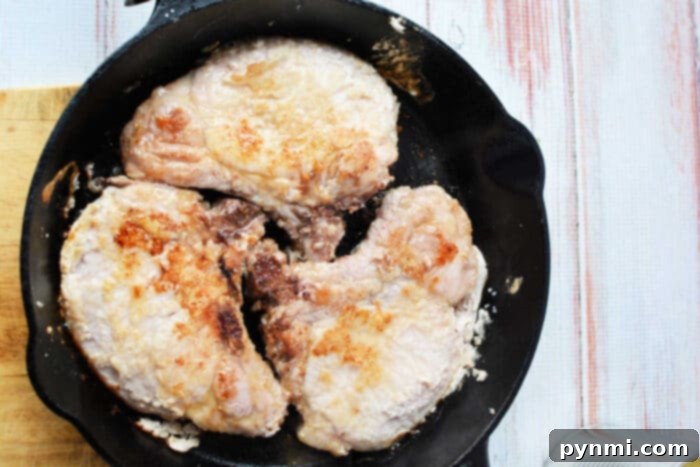 Tropical Pork Chops 5 Four pork chops cooking in a black cast iron skillet on a light wooden surface, perfect for a savory pork and pineapple meal.