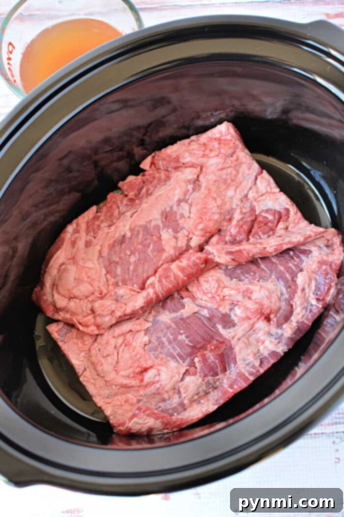 Two raw pieces of beef, ideal for slow cooker skirt steak, are placed inside a black slow cooker, with broth in a measuring cup nearby—perfect for those seeking delicious skirt steak recipes.