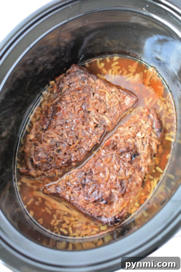 Two pieces of beef brisket cook in a slow cooker with broth and seasonings, just like you would prepare Slow Cooker Skirt Steak for tender, flavorful results.