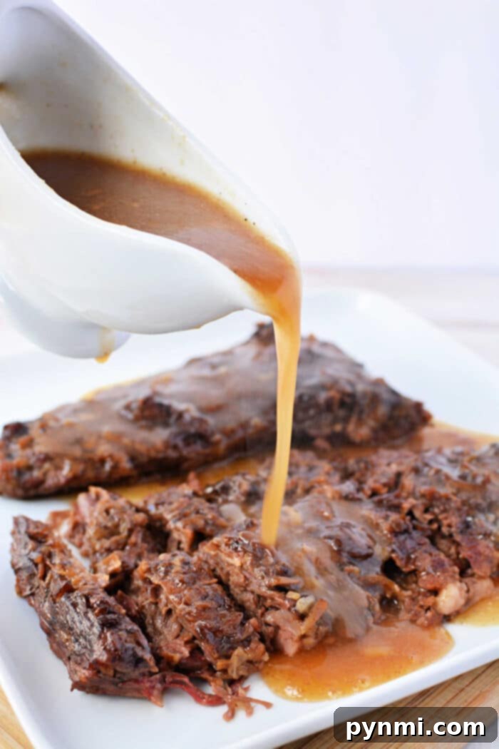 Gravy being poured from a white gravy boat over tender Slow Cooker Skirt Steak, sliced and arranged on a white plate.