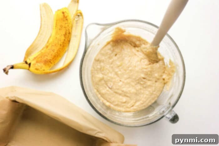 Power-Packed Banana Bread 5 A glass bowl of Protein Banana Bread batter with a spatula sits beside banana peels and a parchment-lined pan, ready to be baked.