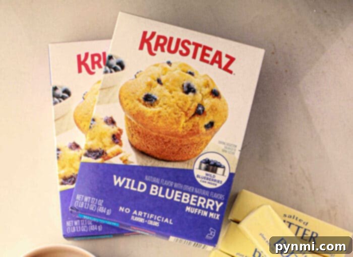Box of Krusteaz Blueberry muffin mix on a counter next to butter packets and another muffin mix box, ready to help you improve your recipe.