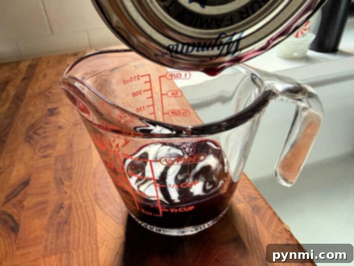 Red liquid being poured from a can into a glass measuring cup on a wooden countertop—perfect for learning how to make blueberry muffin mix better with flavorful additions.