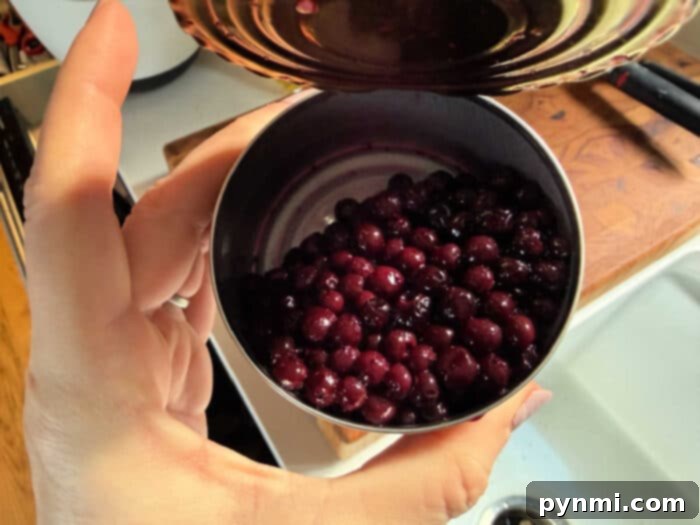 A hand holds an open can filled with dark purple berries over a kitchen sink and cutting board—perfect for learning how to make blueberry muffin mix better.