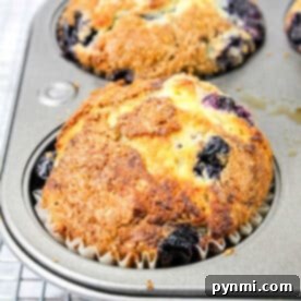 A golden-brown blueberry muffin made with blueberry muffin mix rests in a muffin tin on a cooling rack.