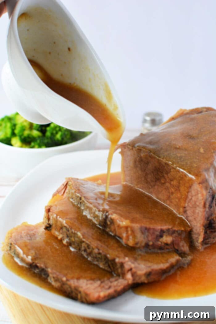 Slow cooker gravy being poured over sliced Beef Bottom Round Roast on a white plate, with broccoli in the background.