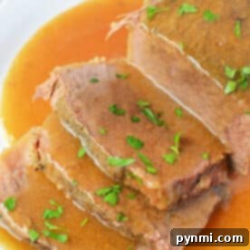 Sliced slow cooker beef bottom round roast with savory gravy and chopped parsley, served on a white plate.