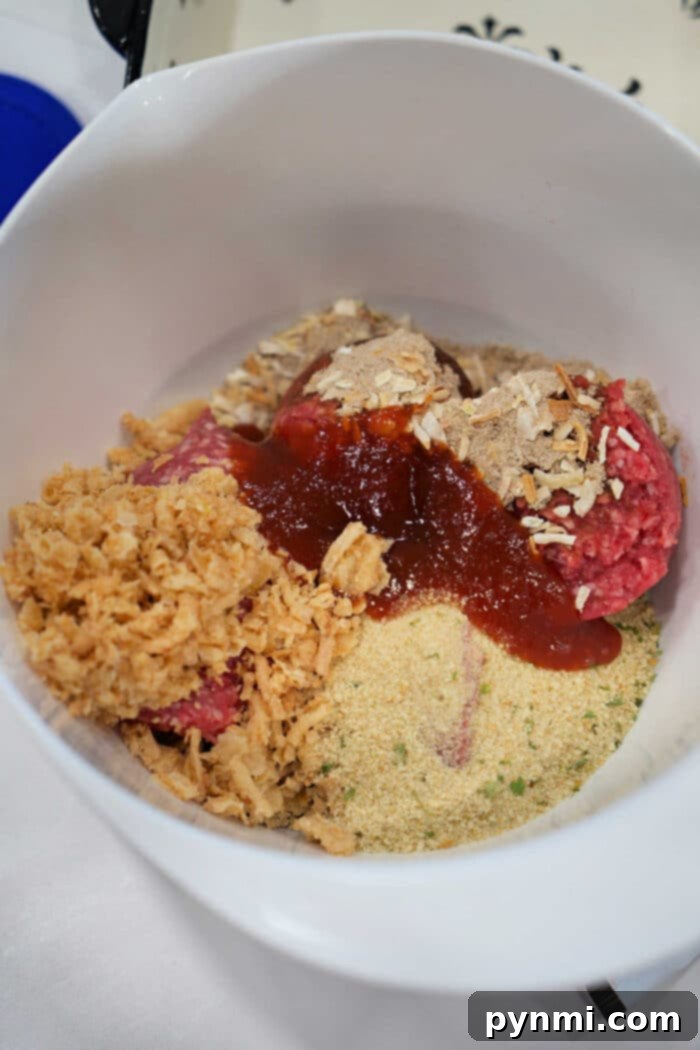 Ultimate BBQ Glazed Meatloaf 4 A colorful array of unmixed meatloaf ingredients meticulously arranged in a bowl, featuring raw ground beef, various breadcrumbs, crushed chips, and a rich sauce—all perfectly set to begin crafting your favorite BBQ meatloaf recipe.