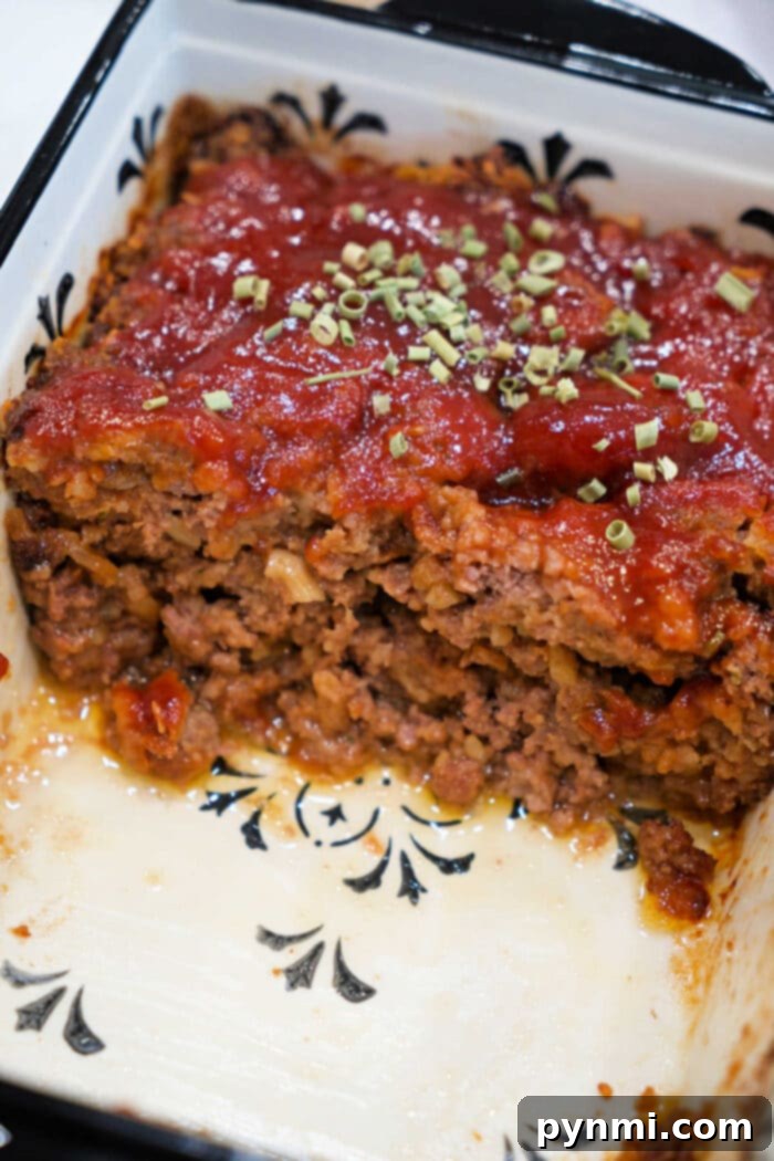 Ultimate BBQ Glazed Meatloaf 6 A beautifully sliced meatloaf, generously topped with a rich tomato sauce and fresh herbs, presented in a stylish white baking dish with a subtle black pattern—perfect for savoring a classic Meatloaf Recipe or indulging in a transformed, savory BBQ Meatloaf.