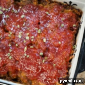 A baked BBQ meatloaf topped with tomato sauce and chopped herbs in a rectangular dish.