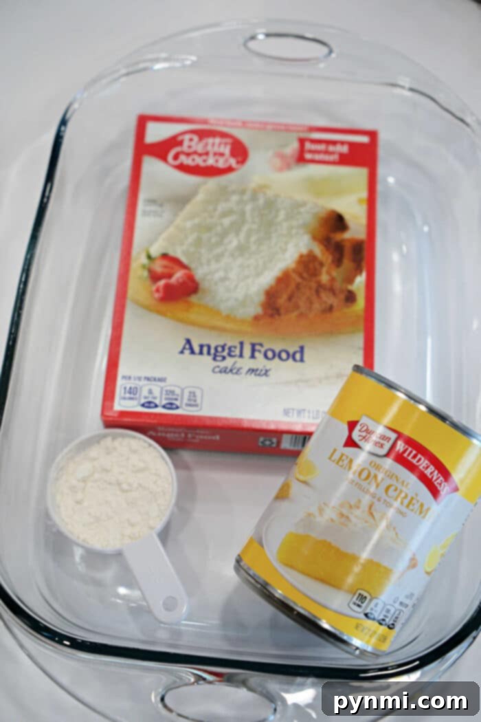Ingredients for easy 2-ingredient lemon angel food cake: a glass baking dish, a box of angel food cake mix, a can of lemon creme pie filling, and a measuring cup, perfectly arranged for dessert preparation.