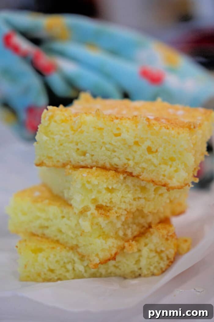 Two pieces of golden lemon angel food cake, perfectly stacked on white parchment paper, resting alongside a soft, colorful kitchen towel, inviting immediate enjoyment of this simple, delicious dessert.
