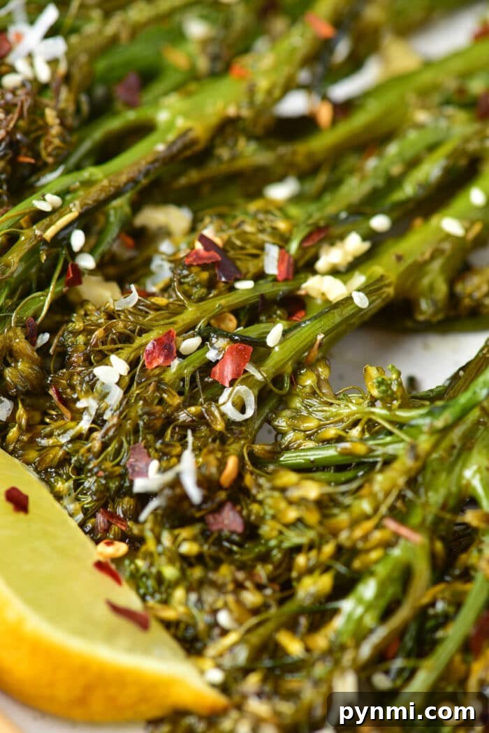 Close-up of oven-roasted broccolini topped with sesame seeds, red pepper flakes, and a lemon wedge.