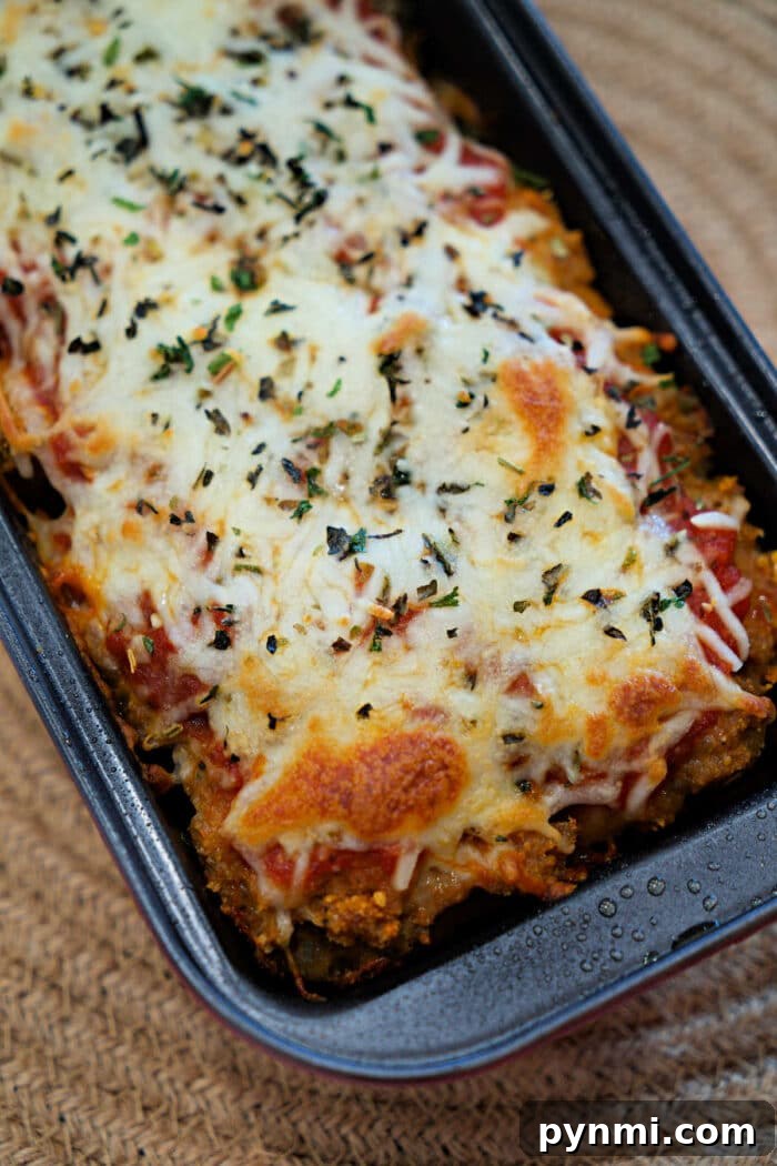 Chicken Parmesan Meatloaf Recipe: Savory Italian-Style Loaf 2 Baked Chicken Parmesan Meatloaf casserole topped with melted cheese and herbs in a rectangular dish on a woven placemat.