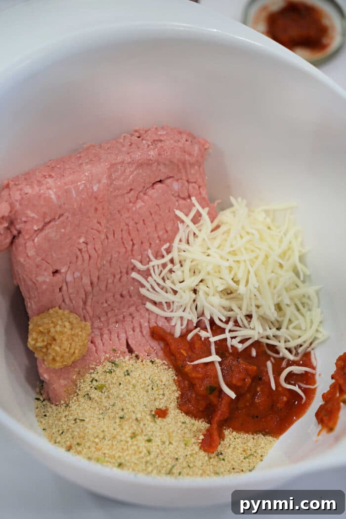 Chicken Parmesan Meatloaf Recipe: Savory Italian-Style Loaf 3 Ground meat, shredded cheese, breadcrumbs, minced garlic, and tomato sauce in a white mixing bowl—perfect for preparing a flavorful Chicken Parmesan Meatloaf.