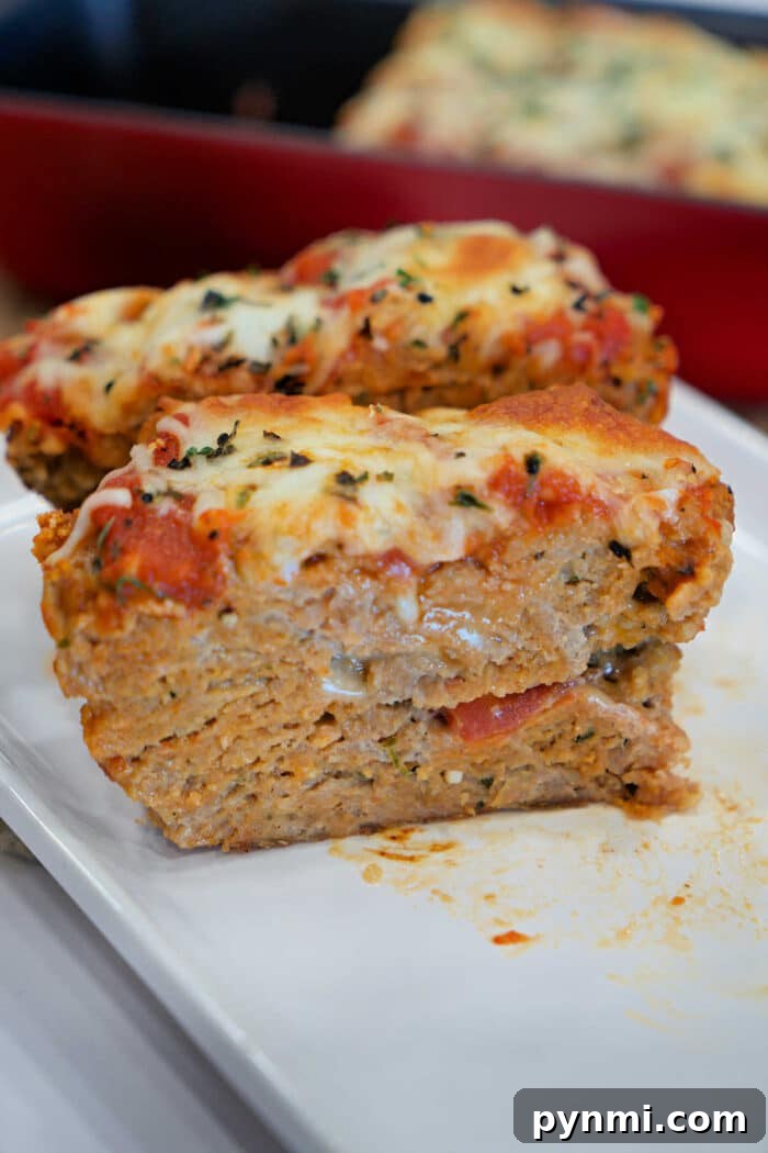 Chicken Parmesan Meatloaf Recipe: Savory Italian-Style Loaf 5 Two slices of cheesy, baked Chicken Parmesan Meatloaf topped with tomato sauce and herbs sit on a white plate.