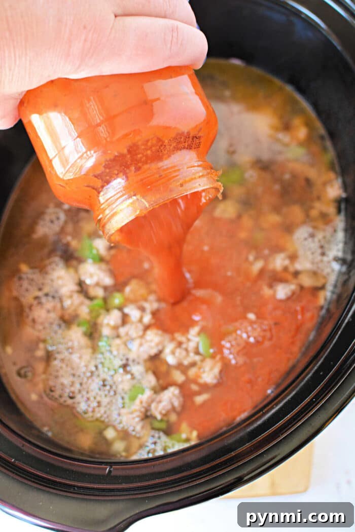 Slow-Cooker Lasagna Soup Recipe for Comforting Weeknight Meals 5 A hand pours tomato sauce from a jar into a Crockpot filled with ground meat and vegetables, perfect for making hearty Lasagna Soup.