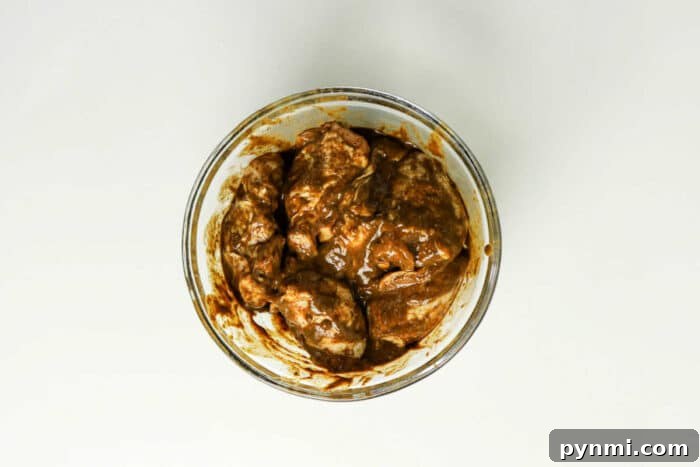 Oven-Baked Jerk Chicken Recipe – Crispy, Flavorful & Authentic 4 Glass bowl with pieces of meat coated in a thick brown jerk chicken marinade, ready for the oven, placed on a white surface—a perfect start to your favorite jerk chicken recipe.