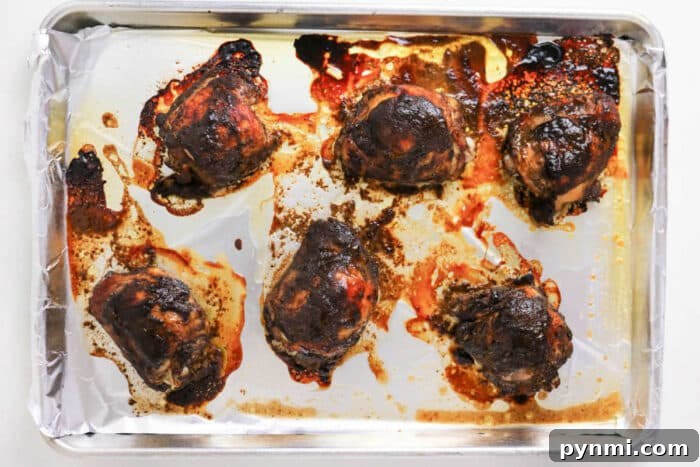 Oven-Baked Jerk Chicken Recipe – Crispy, Flavorful & Authentic 5 Six oven jerk chicken thighs on a foil-lined baking sheet, with browned and crispy skin and flavorful juices around them.