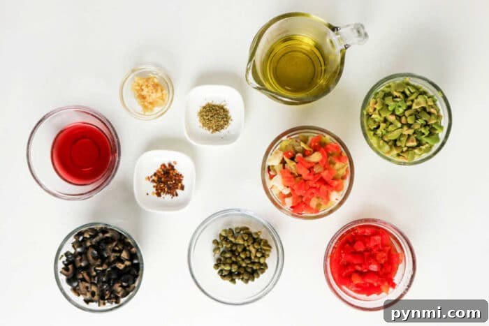 Various small bowls with chopped vegetables, olives, capers, spices, oil, and vinegar arranged on a white surface—perfect ingredients for a classic Muffuletta recipe or homemade olive salad.