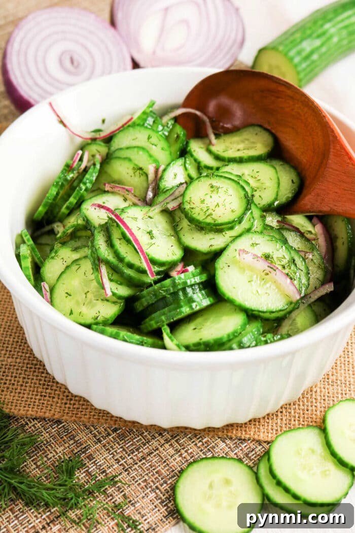 Crisp Cucumber Dill Salad with Creamy Yogurt Dressing 2 Bowl of cucumber salad with crisp red onion slices and fresh dill, all mixed together with a wooden spoon.