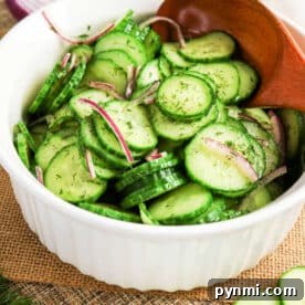 Crisp Cucumber Dill Salad with Creamy Yogurt Dressing 7 Bowl of cucumber salad with crisp red onion slices and fresh dill, all mixed together with a wooden spoon.