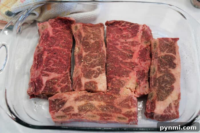 Flavorful Grilled Flanken Short Ribs Recipe for Tender Results 3 Raw, seasoned beef short ribs arranged in a glass baking dish, ready for cooking.