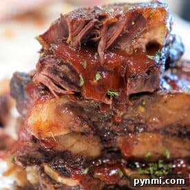 Close-up of stacked, juicy BBQ beef ribs with sauce and herbs on foil.