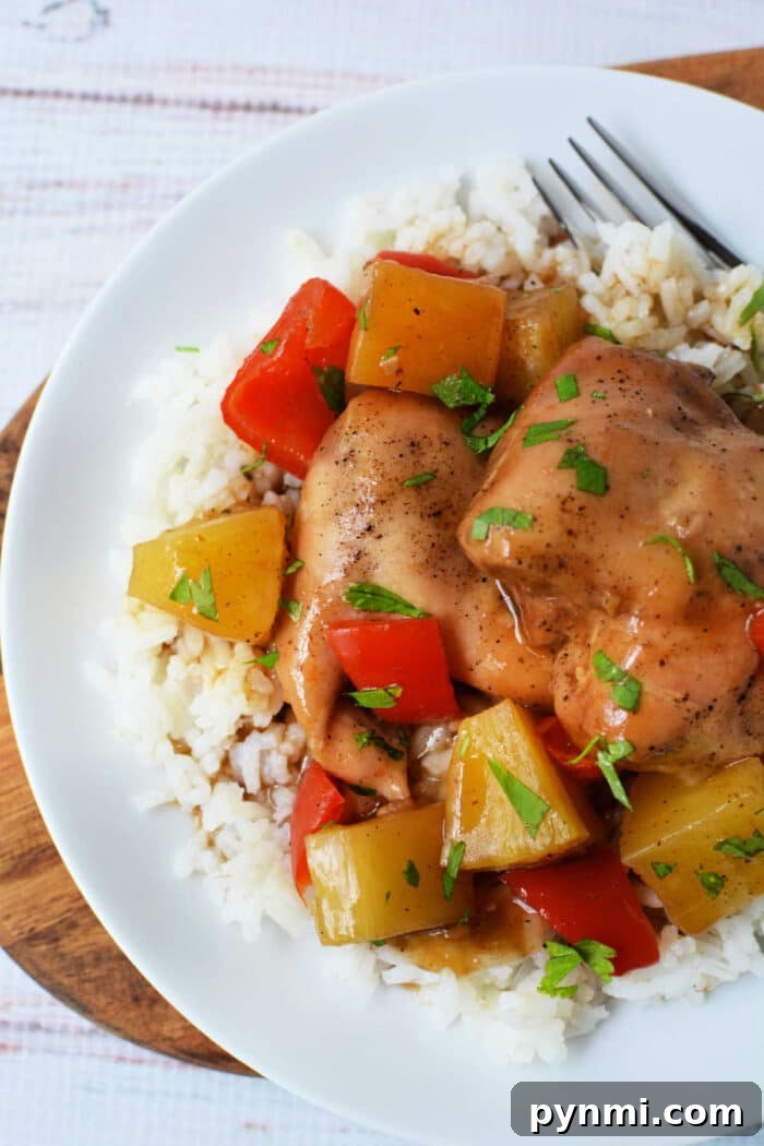 Slow Cooker Pineapple Chicken: Tender, Juicy Crockpot Recipe 6 Slow Cooker Chicken with pineapple, red bell peppers, and savory sauce served over white rice on a white plate with a fork.