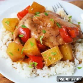 Slow Cooker Pineapple Chicken: Tender, Juicy Crockpot Recipe 7 Slow Cooker Chicken with pineapple chunks and red bell peppers served over white rice on a white plate, finished with a splash of pineapple juice for extra flavor.